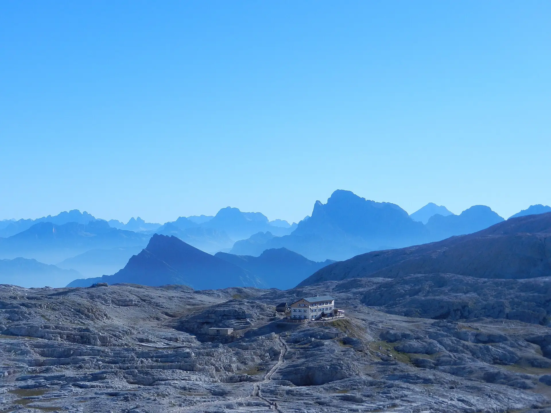 The vast limestone plateau of the Altopiano delle Pale at ~2,600 m — a lunar landscape with a solitary refuge and distant peaks.