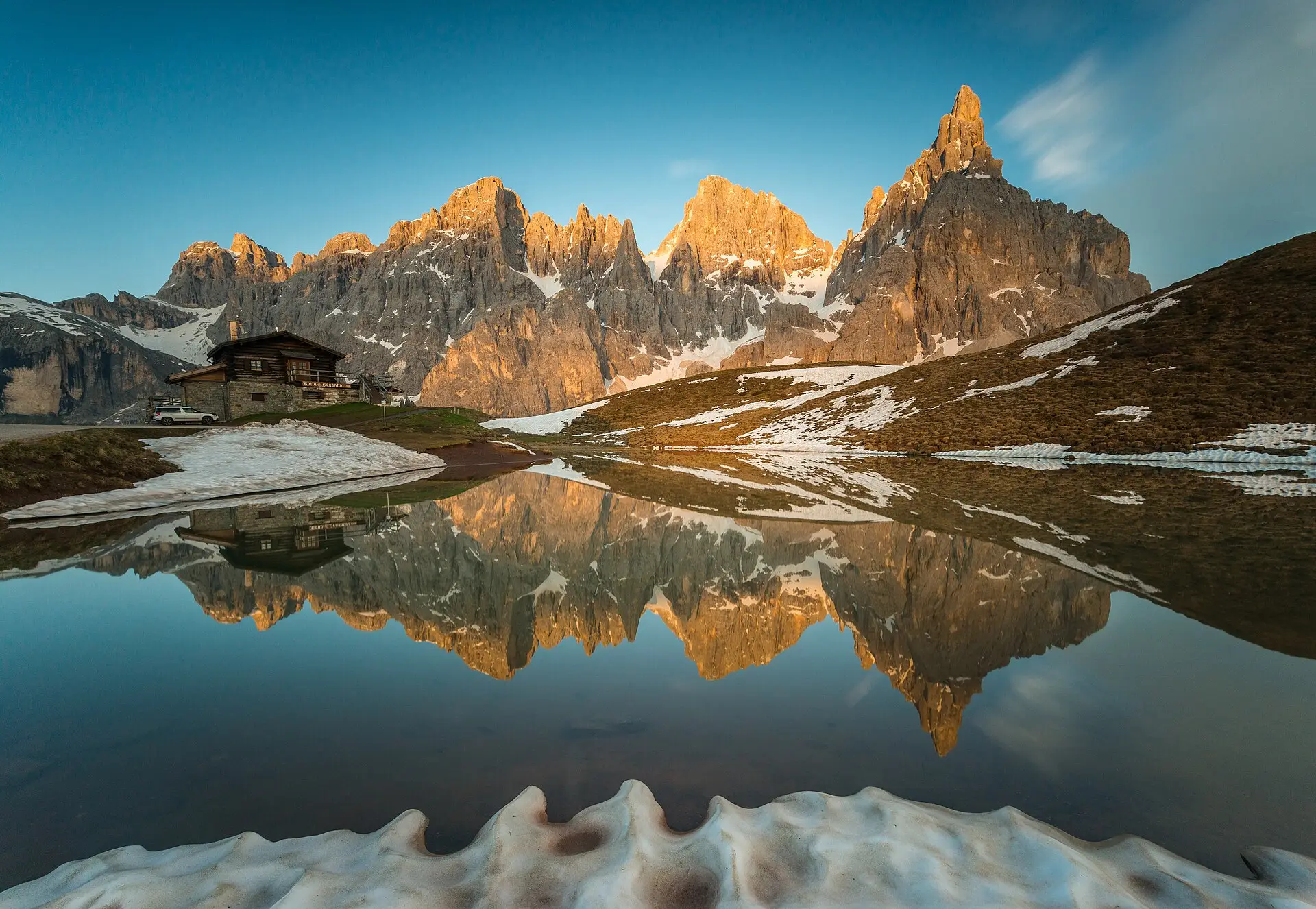 Pale di San Martino peaks glowing in alpenglow, reflected in the tarn at Baita Segantini above Passo Rolle.