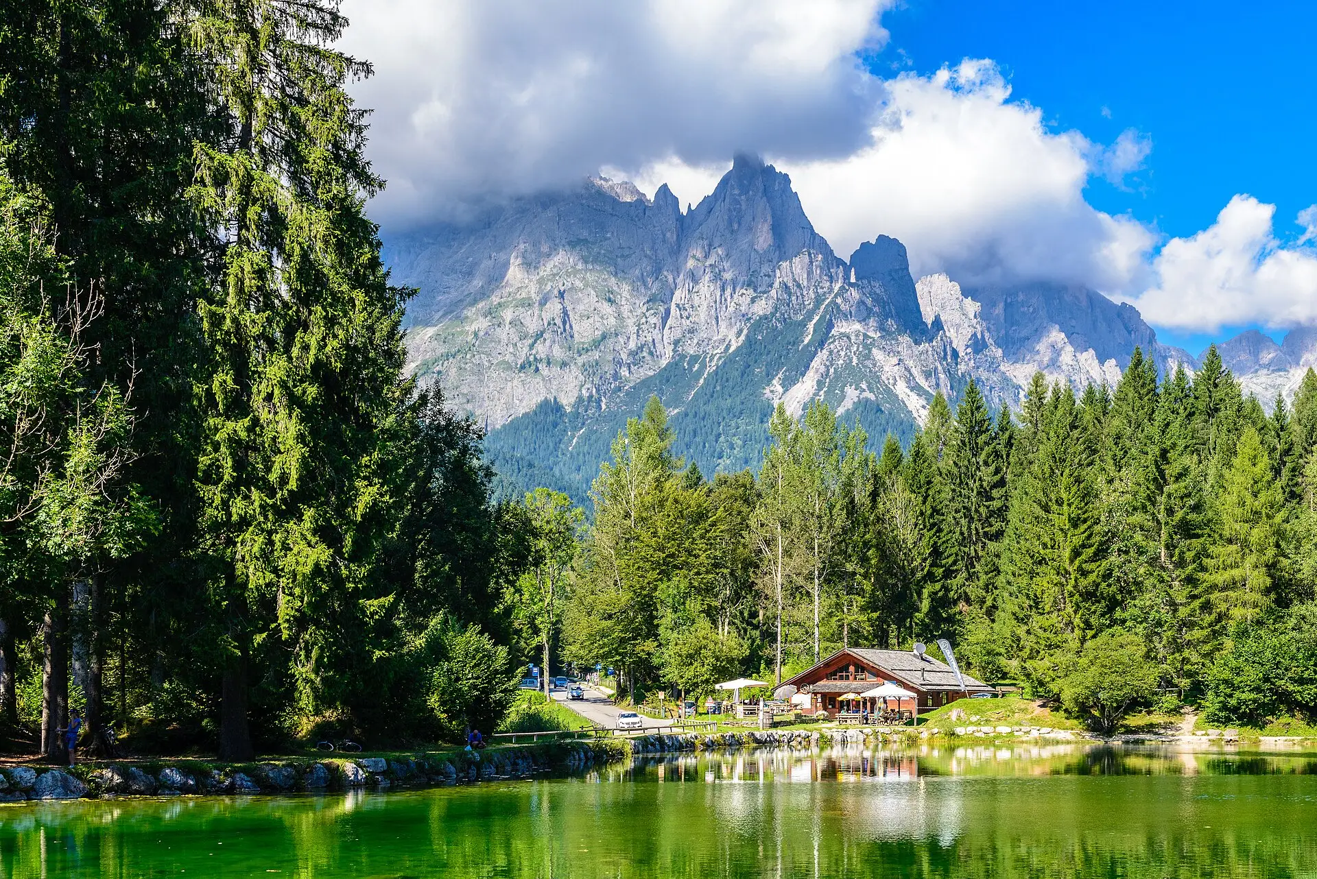 Lago Welsperg in Val Canali — a small green alpine lake with a wooden refuge and dolomite peaks rising behind.