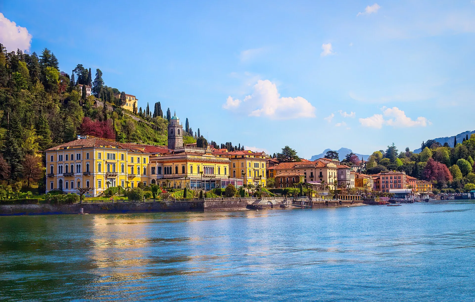 Bellagio waterfront — pastel buildings, a small church campanile, and trees above the lake.